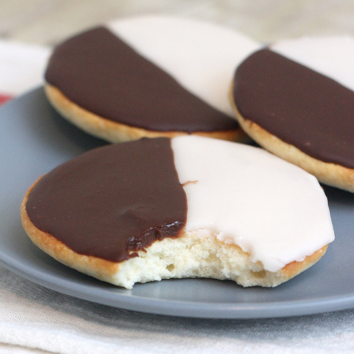 Three black and white cookies; the one appearing in the front has a bite taken out of it.