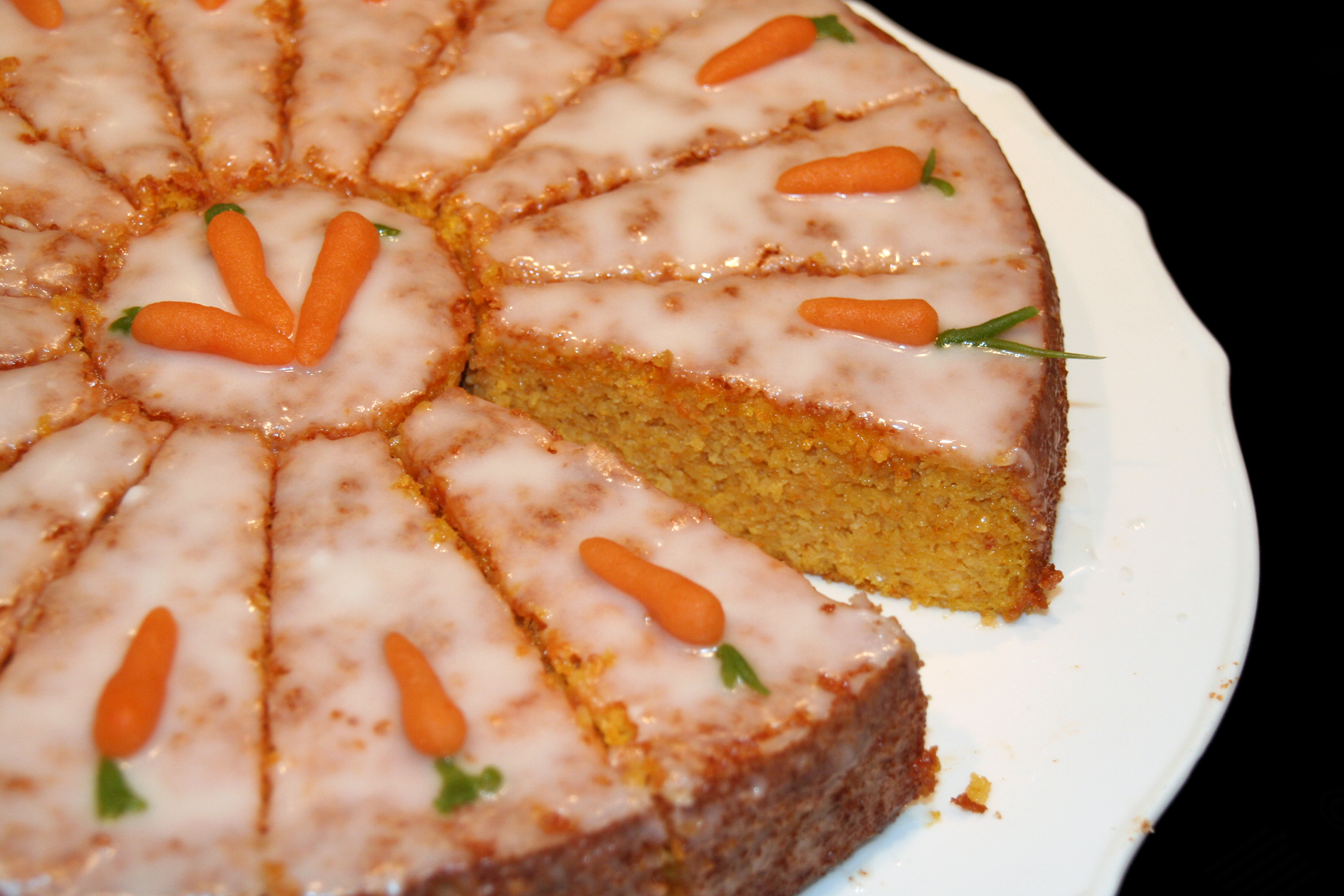 Carrot cake; there is a slice missing. The cake has small carrots made of icing on the top.