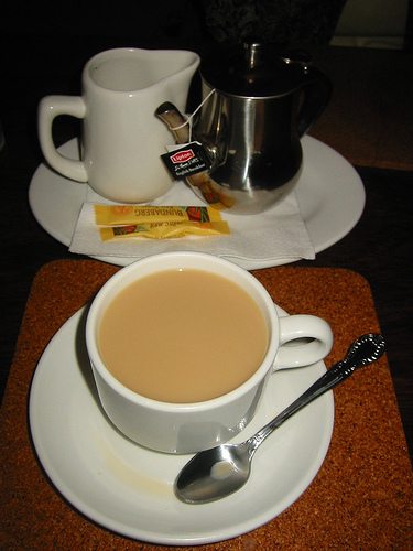 A cup of English breakfast tea served with soy milk; a spoon is on the side of the plate.